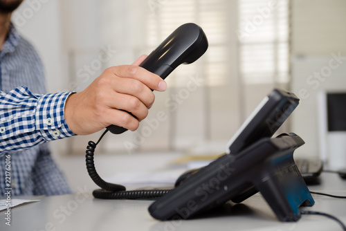 Closeup of businessman dialing making office phonecall, light table background. Corporate male holding telephone handle digital electronic pc connection checking daily data news, online chat talk job.