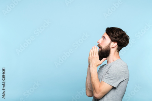 man looking sideways and is amazed or impressed by smth on the left. free space for advertisement or text. portrait of a bearded guy on blue background.