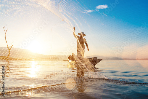 Photo shot of water spatter from fisherman while throwing fishing net on the lake. Silhouette of fisherman with fishing net in morning sunshine.