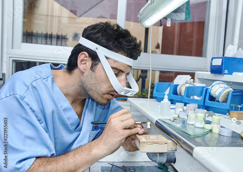 Dental technician working with ceramic dental implants with magnifying glasses