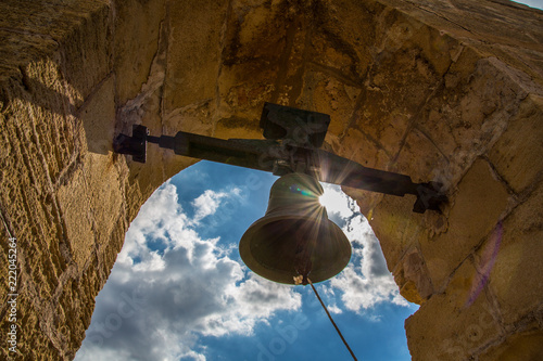 outdoor church bell in front of the shining sun and cloudy blue sky 