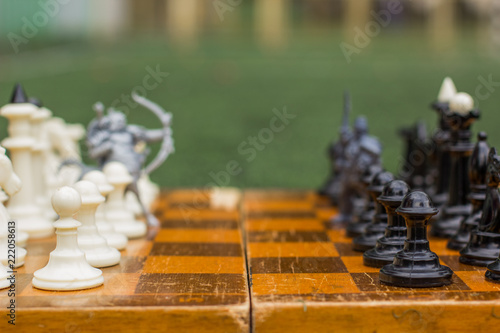 fantasy concept of soft focus black and white classic chess figures and unfocused silhouette of soldier fantasy centaur between their ranks and ready to battle, wooden desk surface, empty copy space