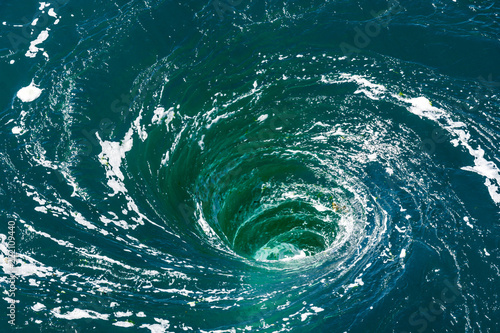 High angle view of a powerful whirlpool at the surface of green water with foam.