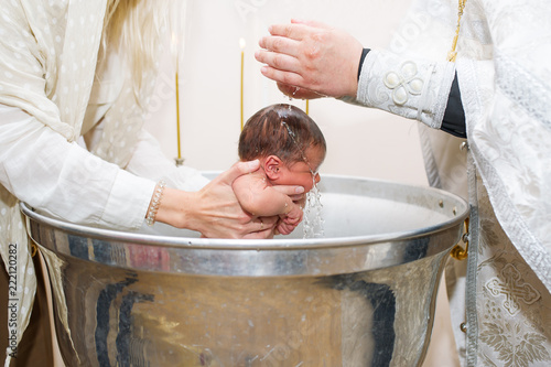 Mother holds child while priest baptizes with holy water