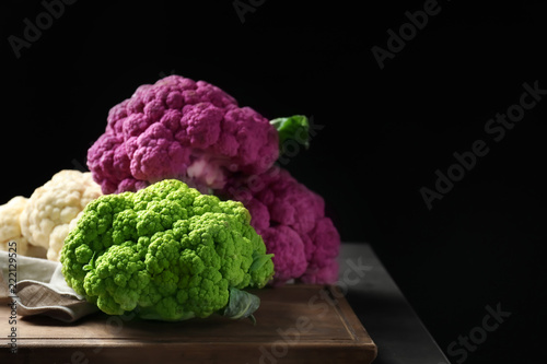 Board with green and purple cauliflower cabbages on table against black background