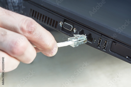 Dłoń mężczyzny wkłada wtyczkę ethernet RJ45 do internetu. Podłączanie internetu przez kabel do komputera wtyczka RJ45