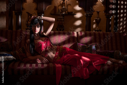 A girl in oriental attire in a dark room in the rays of light.