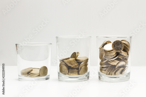 Monedas dentro de hucha de vasos de cristal sobre fondo blanco y gris aislado. Vista de frente. Concepto ahorro. Copy space