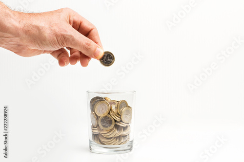Mano de hombre sosteniendo una moneda para que caiga dentro de una hucha con monedas sobre un fondo gris claro. Vista de frente. Concepto ahorro. Copy space