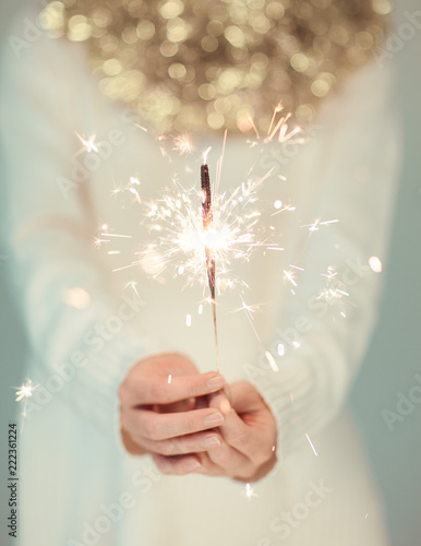 Beautiful woman hands holding sparkler lights, cozy, bright winter sweater with golden christmas garland, can be used as background 