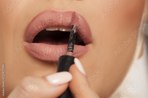 Young woman applying lipgloss on white background