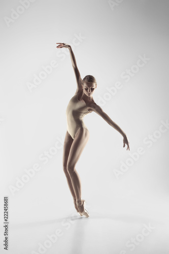 Young graceful female ballet dancer or classic ballerina dancing on white studio. Caucasian model on pointe shoes