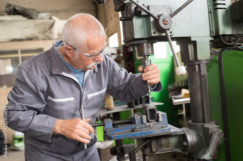 elderly worker watches processing of detail on milling machine