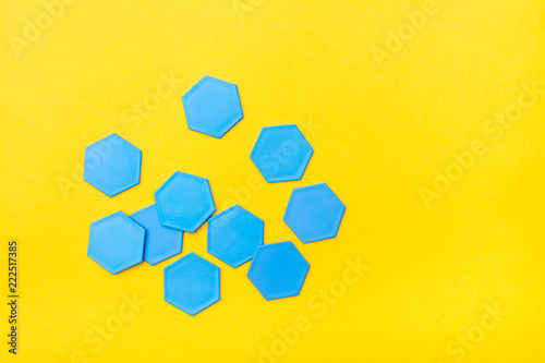 Blue plastic flat hexagons are scattered chaotically on a yellow background. Top View. Copy space