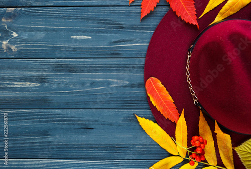 Burgundy or marsala color hat on a gray wooden background with autumn yellow, red leaves and berries. Flat lay, copyspace
