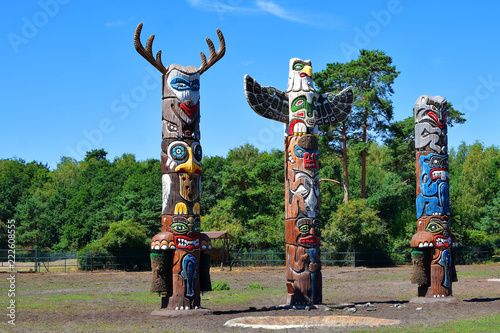 Three colorful wooden totem poles on green trees and blue sky background outdoors in park.