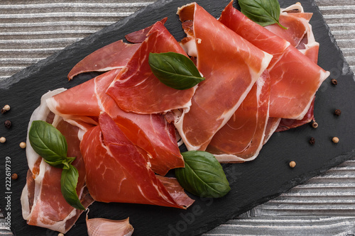 Italian prosciutto crudo or spanish jamon on a stone plate wooden background