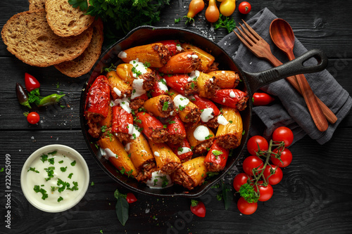 Sausage meat, mince and rice Stuffed sweet mini bell peppers baked in cast iron skillet, pan topped with yogurt and fresh parsley