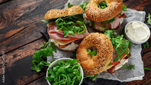 Fresh Bagels Sandwiches with cream cheese, bacon, tomato and green wild rocket on rustic wooden table