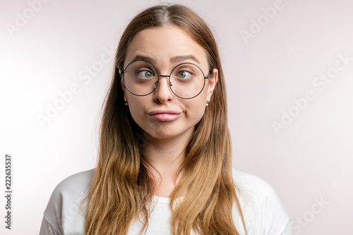 fair-haired attractive girl makes grimace, woman in round glasses crossing eyes student is tired after exams.woman in white T-shirt maks stupid face. closeup portrait