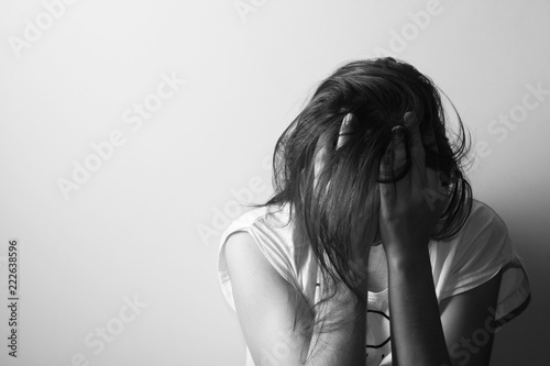 Teenager girl with depression sitting alone on the floor in the dark room. Black and white photography