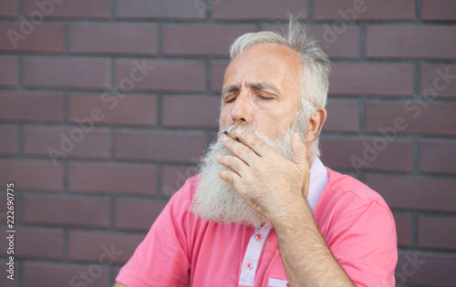 Old man with beard and moustaches in a pink t-shirt smoking.