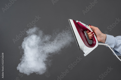 Woman holds an iron with steam on gray background
