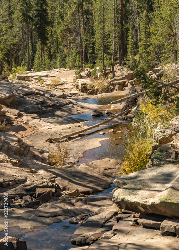 mountain waterfall over striated rock with pine trees