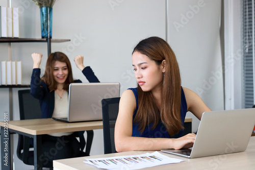 Angry envious Asian business woman looking successful competitor colleague in office.