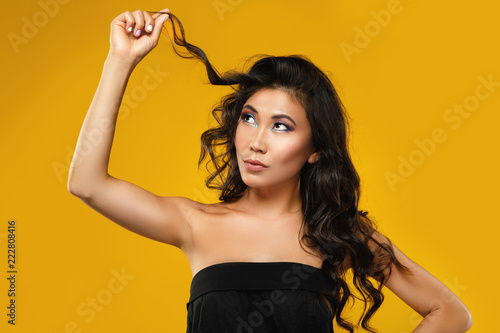 Asian woman with a beautiful curly hair and make-up on yellow background