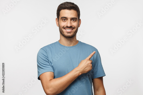 Young man in blue t-shirt pointing right with his finger isolated on gray background