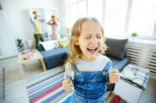 Youthful daughter crying and screaming loudly while being naughty with her shocked parents on background