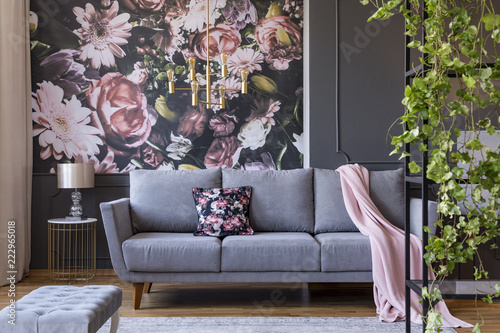 Real photo of a floral living room interior with a wallpaper, sofa and plants
