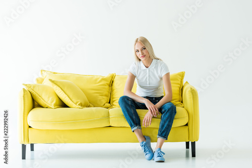 attractive woman sitting on yellow sofa and looking at camera on white