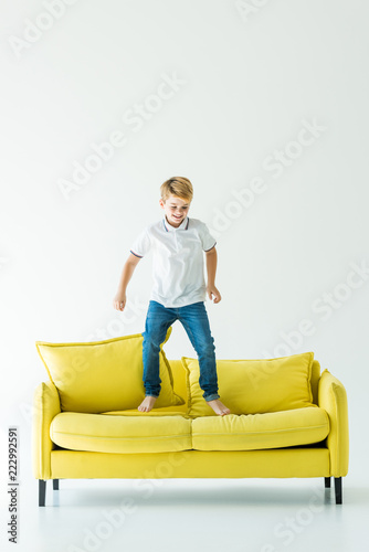 happy adorable boy jumping on yellow sofa on white