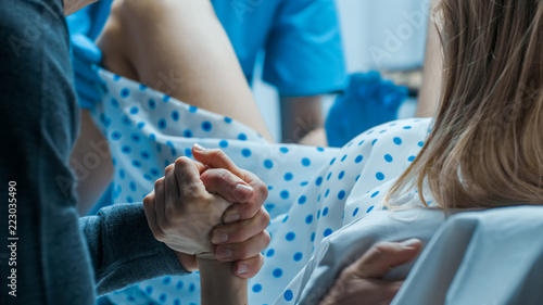 Emergency In the Hospital: Woman Giving Birth, Husband Holds Her Hand in Support, Obstetricians Assisting. Modern Delivery Ward with Professional Midwives.