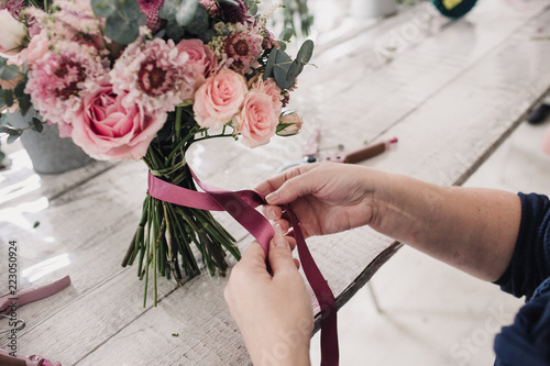 hands of a florist bandage a bouquet with a pink ribbon