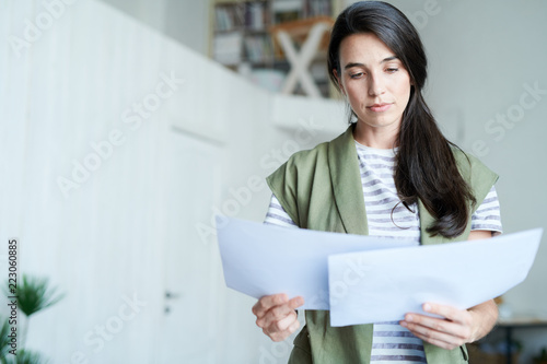 Portrait of brunette young woman holding two documents and reading them, copy space