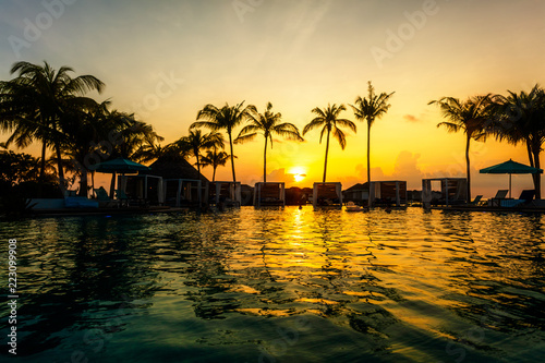 Beautiful tropical sunset at a swimming pool side with palm trees silhouettes and last rays of sun