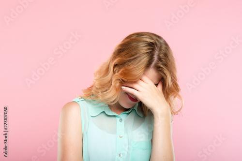 facepalm embarrassment and shame emotion. ashamed smiling girl covering her face with a hand. young beautiful woman portrait on pink background.