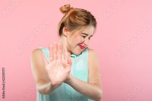 don't want to see it. rejection refusal and denial. young woman putting hands forward as if pushing smth away. portrait of a girl with tightly shut eyes on pink background.