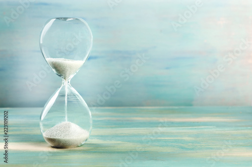 A side view of an hourglass with falling sand, on a teal background with copy space