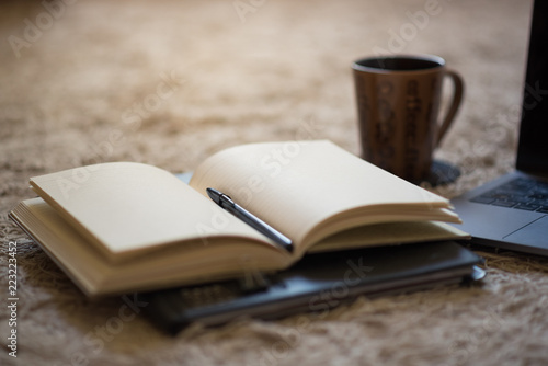 An open journal with pen and warm light illuminating blank pages, coffee mug and laptop in background.