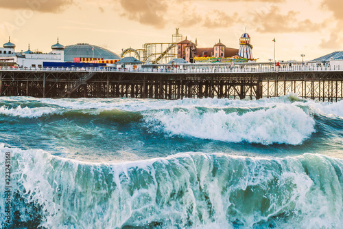 Brighton Pier, Brighton, Sussex, Britain on a storm evening at dusk as the sun is setting. There are high waves and surf on the beach