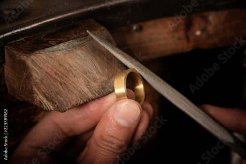 goldsmith hand holds a golden ring on the wooden workbench and works on it with a metal file, close up with copy space