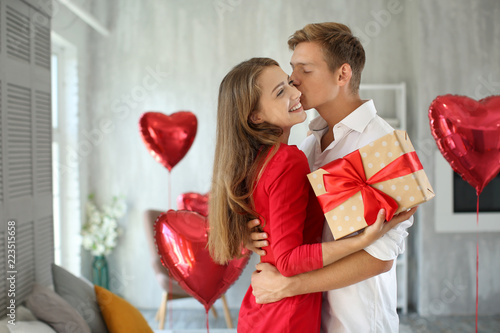 Young couple with gift box hugging at home