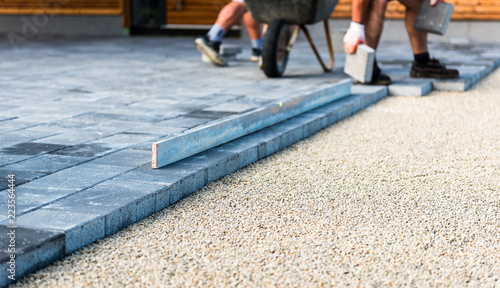 Laying gray concrete paving slabs in house courtyard driveway patio.