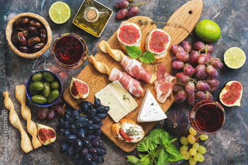 A variety of snacks, prosciutto,grapes, wine, cheese with mold, figs, basil, olives on a rustic background. Top view,flat lay