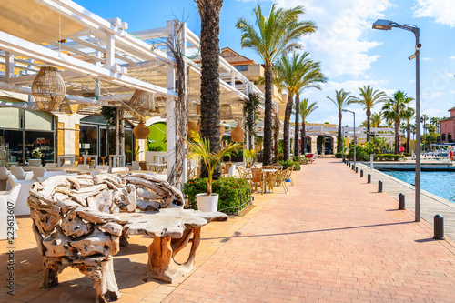 Restaurant tables with chairs in beautiful Sotogrande marina with colorful houses and palm trees on coastal promenade, Costa del Sol, Spain