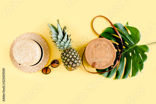 Women's accessories traveler: bamboo bag, straw hat, tropical palm leaves monstera, retro camera on yellow background. The concept of travel. Summer background. Flat lay, top view